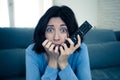 Portrait of a young woman looking scared and shocked watching scary movie on TV Royalty Free Stock Photo