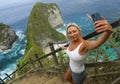 Young attractive and happy blond tourist woman taking selfie at beautiful sea cliff beach viewpoint enjoying exotic holidays Royalty Free Stock Photo