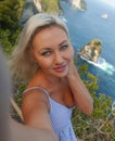 Young attractive and happy blond tourist woman taking selfie at beautiful sea cliff beach viewpoint enjoying exotic holidays Royalty Free Stock Photo