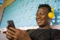 Lifestyle portrait of young attractive and happy cool hipster black afro American man using mobile phone and headset networking on Royalty Free Stock Photo
