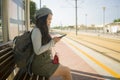 Lifestyle portrait of young attractive and relaxed Asian Chinese woman sitting on bench at train station platform waiting using Royalty Free Stock Photo