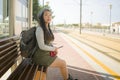 Lifestyle portrait of young attractive and relaxed Asian Korean woman sitting on bench at train station platform waiting cheerful Royalty Free Stock Photo