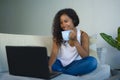 Young attractive and relaxed black african American student woman sitting at home sofa couch networking with laptop computer drink