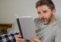 Lifestyle portrait of young attractive and relaxed man at home lying comfortable on bed wearing  pajamas reading a book enjoying Royalty Free Stock Photo