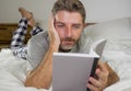 Lifestyle portrait of young attractive and relaxed man at home lying comfortable on bed wearing  pajamas reading a book enjoying Royalty Free Stock Photo