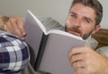 Lifestyle portrait of young attractive and relaxed man at home lying comfortable on bed wearing  pajamas reading a book enjoying Royalty Free Stock Photo