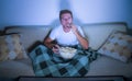 Lifestyle portrait of young attractive relaxed man watching movie on television eating popcorn sitting late night at living room s Royalty Free Stock Photo