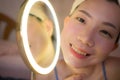 Lifestyle portrait of young beautiful and happy Asian woman applying makeup and beauty facial treatment looking in mirror at home Royalty Free Stock Photo