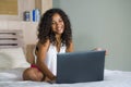 Lifestyle portrait of young beautiful and happy black hispanic woman at home bedroom sitting cheerful on bed networking using lapt Royalty Free Stock Photo