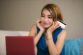 Lifestyle portrait of young beautiful and happy girl at home living room holding credit card using laptop computer for banking an Royalty Free Stock Photo