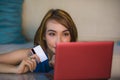 Lifestyle portrait of young beautiful and happy girl at home living room holding credit card using laptop computer for banking an Royalty Free Stock Photo