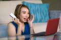 Lifestyle portrait of young beautiful and happy girl at home living room holding credit card using laptop computer for banking an Royalty Free Stock Photo