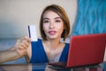 Lifestyle portrait of young beautiful and happy girl at home living room holding credit card using laptop computer for banking an Royalty Free Stock Photo