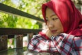 Lifestyle portrait of young beautiful and relaxed Asian Indonesian Muslim girl sitting outdoors wearing traditional islamic hijab Royalty Free Stock Photo