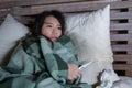 Young beautiful sick and exhausted Asian Japanese woman suffering cold and flu holding thermometer having temperature lying on bed Royalty Free Stock Photo