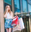 Lifestyle portrait young blonde girl, with shopping bags walking out from shop and talking by mobile phone Royalty Free Stock Photo