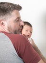 Lifestyle portrait of young father holding and kissing his daughter- an adorable and beautiful newborn baby girl portraying sweet