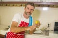 Lifestyle portrait of young handsome and happy man in red apron peeling potato preparing vegetables salad smiling cheerful in home Royalty Free Stock Photo