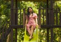 Lifestyle portrait of young happy and beautiful Asian Chinese woman in sweet Summer dress playing on slide at city park smiling Royalty Free Stock Photo