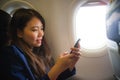 Young happy and beautiful Asian Chinese woman traveling for business inside airplane cabin smiling cheerful using mobile phone in