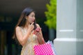 Young happy and beautiful Asian Chinese woman walking on the street carrying shopping bags using mobile phone searching online for Royalty Free Stock Photo