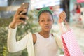 Young happy and beautiful black African American woman holding shopping bags taking selfie with mobile phone buying at mall Royalty Free Stock Photo