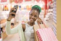 Young happy and beautiful black African American woman holding shopping bags taking selfie with mobile phone buying at mall Royalty Free Stock Photo