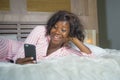 Young happy and beautiful black African American woman in pajamas lying relaxed smiling cheerful and fresh using internet mobile Royalty Free Stock Photo