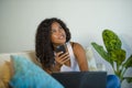 Lifestyle portrait of young happy and beautiful black african American woman using internet mobile phone while working on laptop c Royalty Free Stock Photo