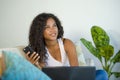 Lifestyle portrait of young happy and beautiful black afro American woman using internet mobile phone while working on laptop comp Royalty Free Stock Photo
