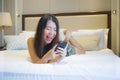 Young happy pretty Asian Korean woman at home or hotel room lying on bed relaxed smiling using internet online dating app texting Royalty Free Stock Photo