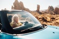 Lifestyle portrait of a young woman enjoying road trip on the desert valley, getting out the convertible car on the Royalty Free Stock Photo