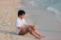 Lifestyle relaxed young Asian man with laptop sitting on the beach. Summer vacation concept. Royalty Free Stock Photo