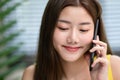 Lifestyle scene close up Asian young woman close her eye lit and smile while holding a smartphone and talking in the natural