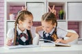 Schoolgirl doing task sitting at desk, another girl doing bunny ears for her and laughing Royalty Free Stock Photo