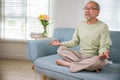 senior man sitting on sofa in living room holding hands in mudra practicing home Royalty Free Stock Photo