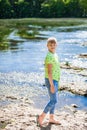 Portrait of little smiling girl child walking outdoor near calm lake at sunny day in spring. Teen is wearing jeans and green shirt