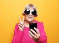 Lifestyle, tehnology and people concept: Elderly lady holding a smartphone making v-sign