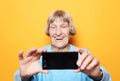 Lifestyle, tehnology and people concept: grandma smiles and takes a selfie over yellow background