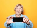 Lifestyle, tehnology and people concept: grandma smiles and takes a selfie over yellow background