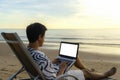 Lifestyle of young Asian man blogger working and using keyboard on laptop while sitting on the beautiful beach, freelance travel Royalty Free Stock Photo