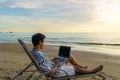 Lifestyle of young Asian man blogger working and using keyboard on laptop while sitting on the beautiful beach, freelance travel Royalty Free Stock Photo