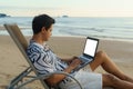 Lifestyle of young Asian man blogger working and using keyboard on laptop while sitting on the beautiful beach, freelance travel Royalty Free Stock Photo