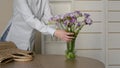 A woman drops a Bouquet of lilac Spring Flowers into a Vase of Water and leaves.