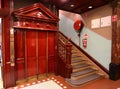 Ornate elevator decorated with wood classical pediment, frieze and pilasters next to decorative balustrade and stairs