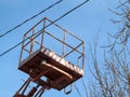 Lift-platform of the aerial device between electrical wires and bare branches of a tree against a blue sky. The concept of work in Royalty Free Stock Photo