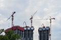 Lift tower cranes on construction site against background of the blue sky, houses new buildings near a residential area Royalty Free Stock Photo