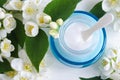 Ligh blue glass jar with facial cream/mask and jasmine blossom flowers background. Copy space.