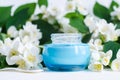 Ligh blue glass jar with facial cream/mask and jasmine blossom flowers background.