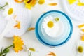 Ligh blue glass jar with white facial cream/mask. ÃÂ¡hamomile and calendula flowers on the white background.